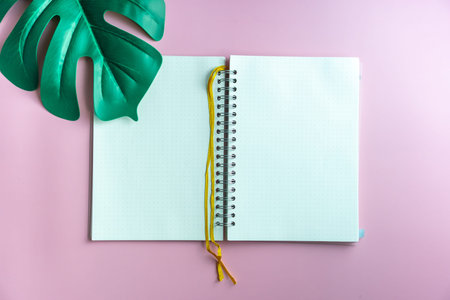 Top view of blank space white notebook and pen with tropical leaf as frame background.
