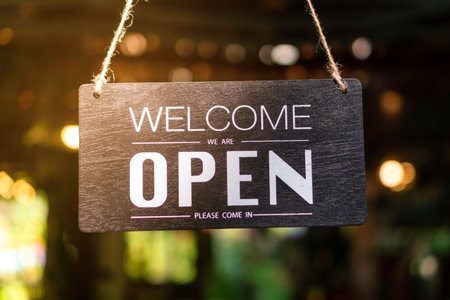 A business sign that says open on cafe or restaurant hang on tree at entrance of shop with sun light...
