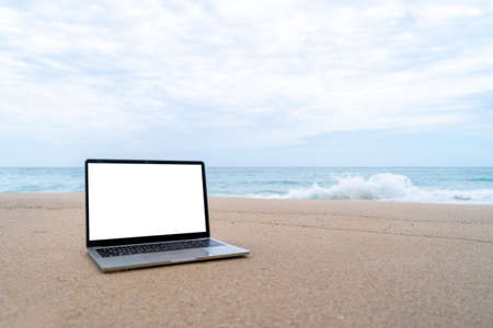 Laptop on sand at summer beach in background with white screen.の写真素材