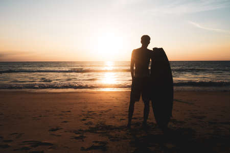Silhouette of surfer man carrying their surfboards on sunset beach with sun light  backgroundの写真素材