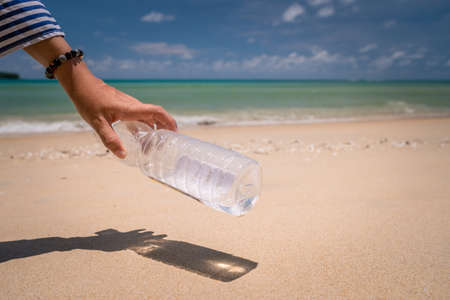 Hand pick up empty water bottle or trash at beautiful beach. Environment Global warming issue.の写真素材
