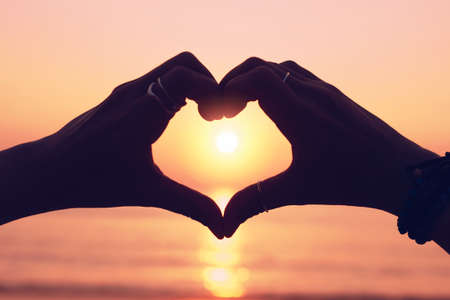 Woman hand do heart shape on sunset sky and bokeh background. love valentine day concept.の写真素材