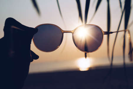 Woman hold sunglasses on sunset beach summer background with sunlight and flare.の写真素材