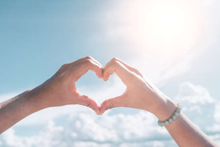 Woman hand do heart shape on blue sky and beach background.の写真素材