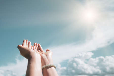 Woman hands place together like praying in front of nature blue sky background.の写真素材