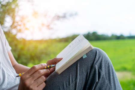 In a public park, a man is handwriting in a small white memo pad to make a note of something he doesn't want to forget or to make a to-do list for the future concept.の写真素材