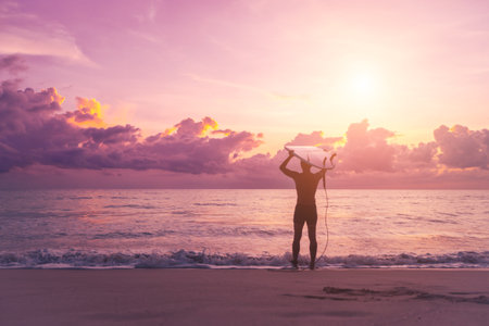 Young man with surfboard on sunset summer tropical beach background.の写真素材