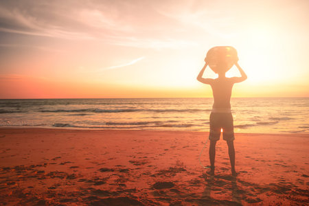Young man with surfboard on sunset summer tropical beach background.