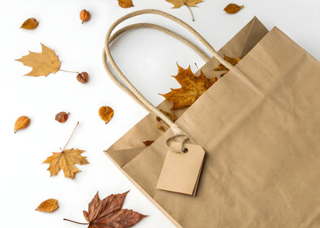 Autumn leaves and paper bag create a seasonal fall shopping theme on white backgroundの素材