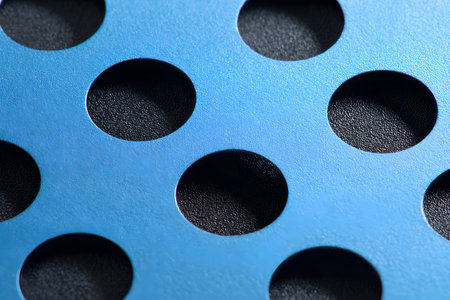 Close-up of a blue metal sheet with circular perforations for industrial useの素材