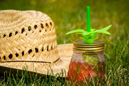 A refreshing cocktail drink in a glass jar and a straw hat in a grass yard.の写真素材