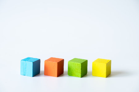 Minimal composition of blue, orange, green, and yellow wooden cubes lined up in a row on a white background, representing creativity, learning, and simplicity.の写真素材