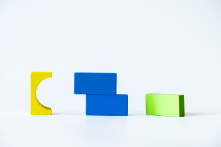 Assorted yellow, green, and blue wooden blocks arranged in an abstract layout on a clean white background, highlighting creativity and simplicity.の写真素材