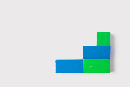 Four rectangular wooden blocks, in shades of blue and green, arranged in an L-shaped pattern on a clean white background in a minimal geometric style.の写真素材