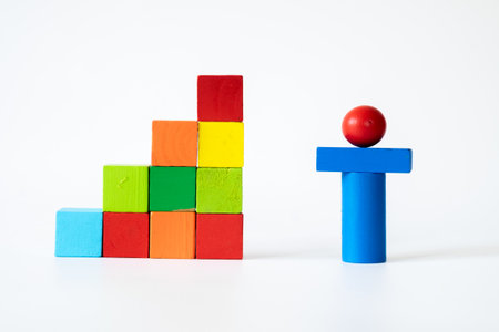 Creative arrangement of colorful wooden cubes in a staircase pattern beside a blue toy figure with a red sphere on white background, symbolizing growth, achievement, and learning.の写真素材