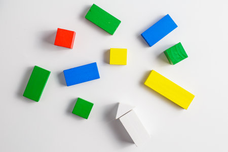 Multiple colorful wooden blocks in various shapes, including rectangles, squares, and one white arrow, randomly arranged on a clean white background.の写真素材