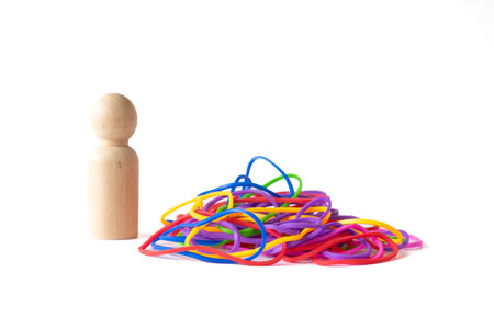 A wooden peg doll stands beside a pile of colorful rubber bands on a white background, symbolizing individuality and connection in a minimalist conceptual composition.の写真素材