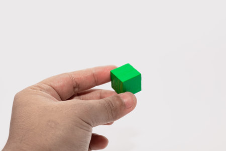 A hand holding a green wooden cube against a clean white background, suitable for education, creativity, and learning themes.の写真素材