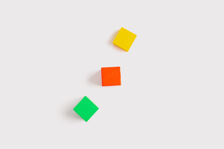 Three colorful wooden cubes, yellow, red and green, arranged diagonally on a clean white background in a minimal and geometric flat lay.の写真素材