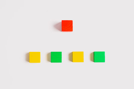 One red wooden cube is centered above a row of alternating yellow and green cubes on a clean white background, captured in a simple, minimalist composition.の写真素材