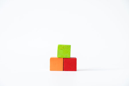Three colorful wooden cubes in green, orange, and red stacked in a simple pyramid arrangement on a clean white background, symbolizing creativity and learning.の写真素材