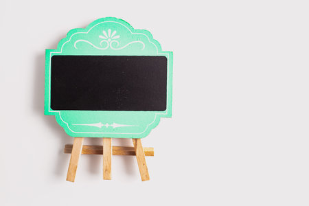 A decorative green-framed mini blackboard with ornate white detailing, standing on a wooden easel against a clean white background.の写真素材