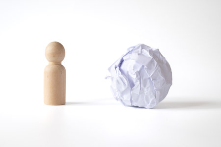 A wooden peg doll and a large crumpled paper ball displayed on a white background, conceptualizing problem-solving, frustration, and new ideas in a minimalist visual metaphor.の写真素材