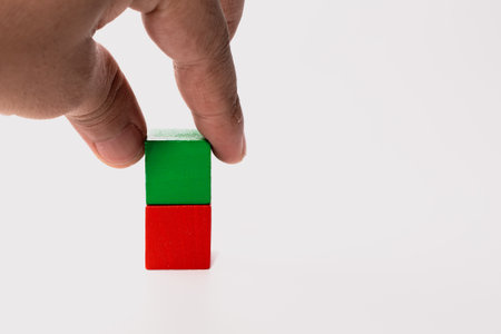A hand gently touches a green and red wooden block stacked vertically on a white background.の写真素材