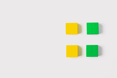 Four small wooden cubes, alternating yellow and green, arranged in a 2x2 square grid pattern on a clean white background for a minimalist, modern look.の写真素材