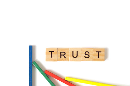 Lettered wooden blocks spelling "TRUST" rest above four colored sticks arranged graph-style, symbolizing trust, teamwork, and growth on a clean white background.の写真素材