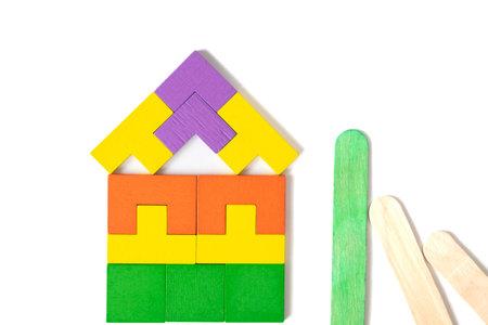 A colorful house made of geometric blocks stands beside green and wooden popsicle sticks on a white background, symbolizing creativity, eco-friendliness, and building ideas.の写真素材