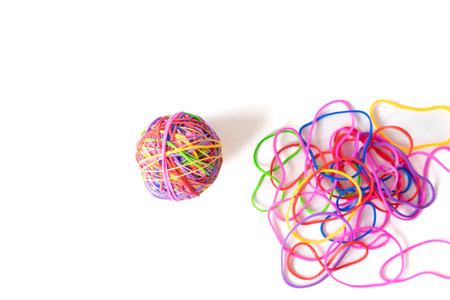 Compact colorful rubber ball beside scattered tangled elastic bands on white background, contrasting...