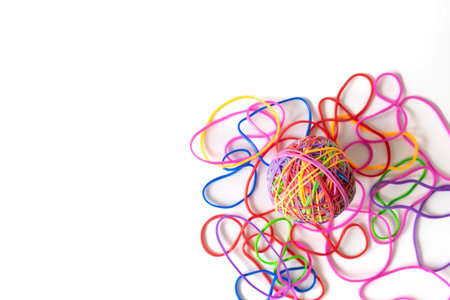 A vibrant ball made of multicolored rubber bands sits on a white background, with loose bands...