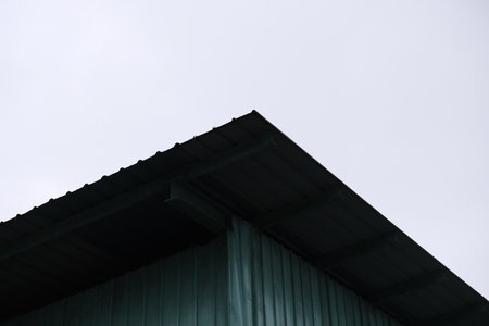 Sharp diagonal roof edge of green corrugated metal building set against pale overcast skyの写真素材