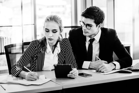 Black and white design man and women working on laptop at their desk with manager supervising the work. Business people working in a small office.の写真素材
