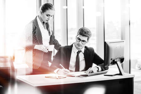 Black and white design man and women working on laptop at their desk with manager supervising the work. Business people working in a small office.の写真素材