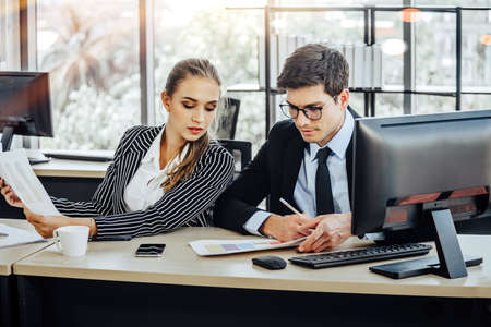 People working on laptop at their desk with manager supervising the work. Business people working in a small office.の写真素材