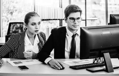 Black and white design man and women working on laptop at their desk with manager supervising the work. Business people working in a small office.の写真素材