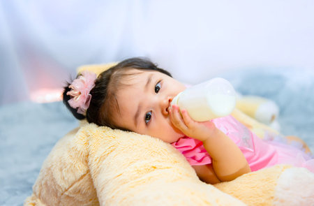 1 year old cute baby girl in a pink dress is playing with teddy bear on the bed in Bangkok Thailand.