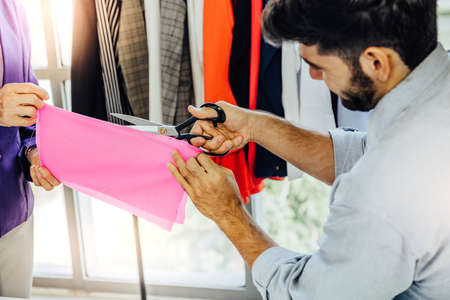Creative Garment Design Tailoring Service Concept. Cute Professional Sewer Measuring Male Bearded Model Waist or Hip. Smiling Outfit Designer Taking Man Measurement for Formal Suit with Tape Meterの写真素材