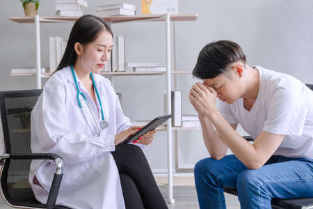 mental people concept. The young doctor's psychologist is working by tablet See reports of man mental patients at officeの写真素材