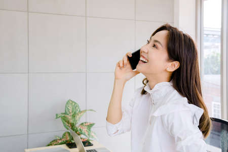 young businesswoman in office concept. she is beautiful, confident, smiling, professional corporate working in financial company Using mobile technology, tablet, cell phone, she happy and drink coffeeの写真素材