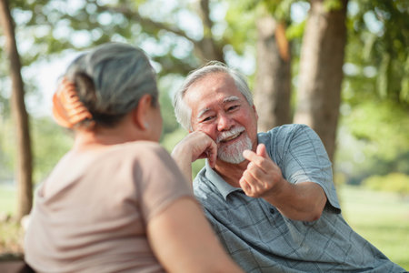 Close up, Asian senior couple having a good time while sitting outdoors in the park. Cheerful have a...