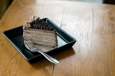 Chocolate Crepe cake and fork in black square dish on wood tableの写真素材