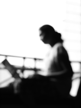 out of focus black and white silhouette image of a girl working with laptopの写真素材