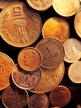 Closeup portrait of bunch of coins from various nationalities including US 5 cents &amp; 1 dime with FDR, Indian 1 &amp; 10 rupee placed on black background with evening golden sunlight reflectionsの写真素材