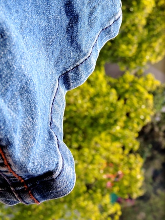 Bottom or hem of a vibrant blue denim jeans having gentle wrinkles in bright daylight with stitching visible and vibrant green vegetation blurred in the backgroundの写真素材