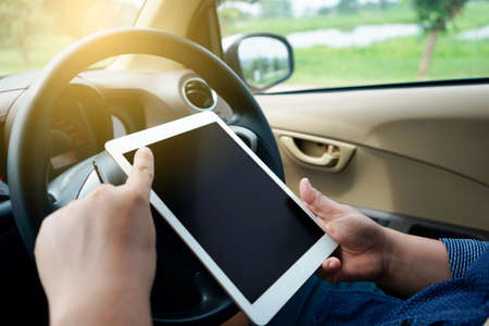 A man sitting in a car, holding and using a tabletの写真素材
