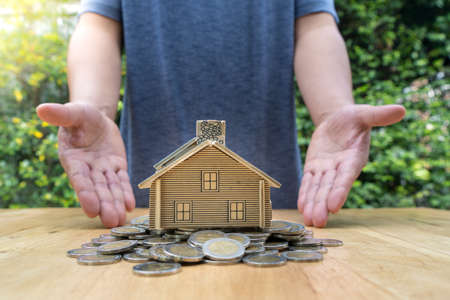 Small house standing on a pile of coins. With the hands of men The concept of buying a homeの写真素材