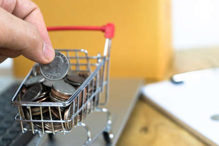 Men's Hand Picking Coins in a trolley on a laptop keyboard and contract. Ideas about online shoppingの写真素材